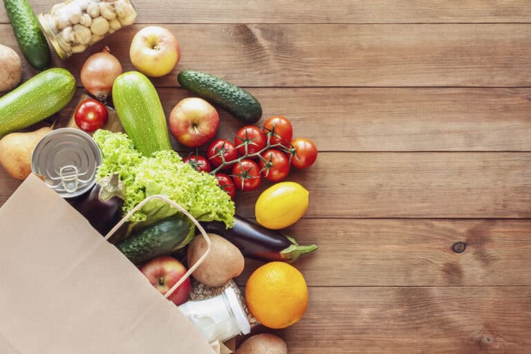 a paper bag filled with fruits and vegetables on a wooden table
